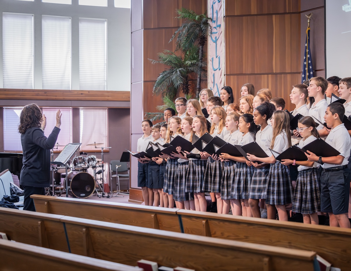 The GVCA Junior High choir sings in the Sanctuary at Chapel. They are all following the Choir Director's instructive hand movements.