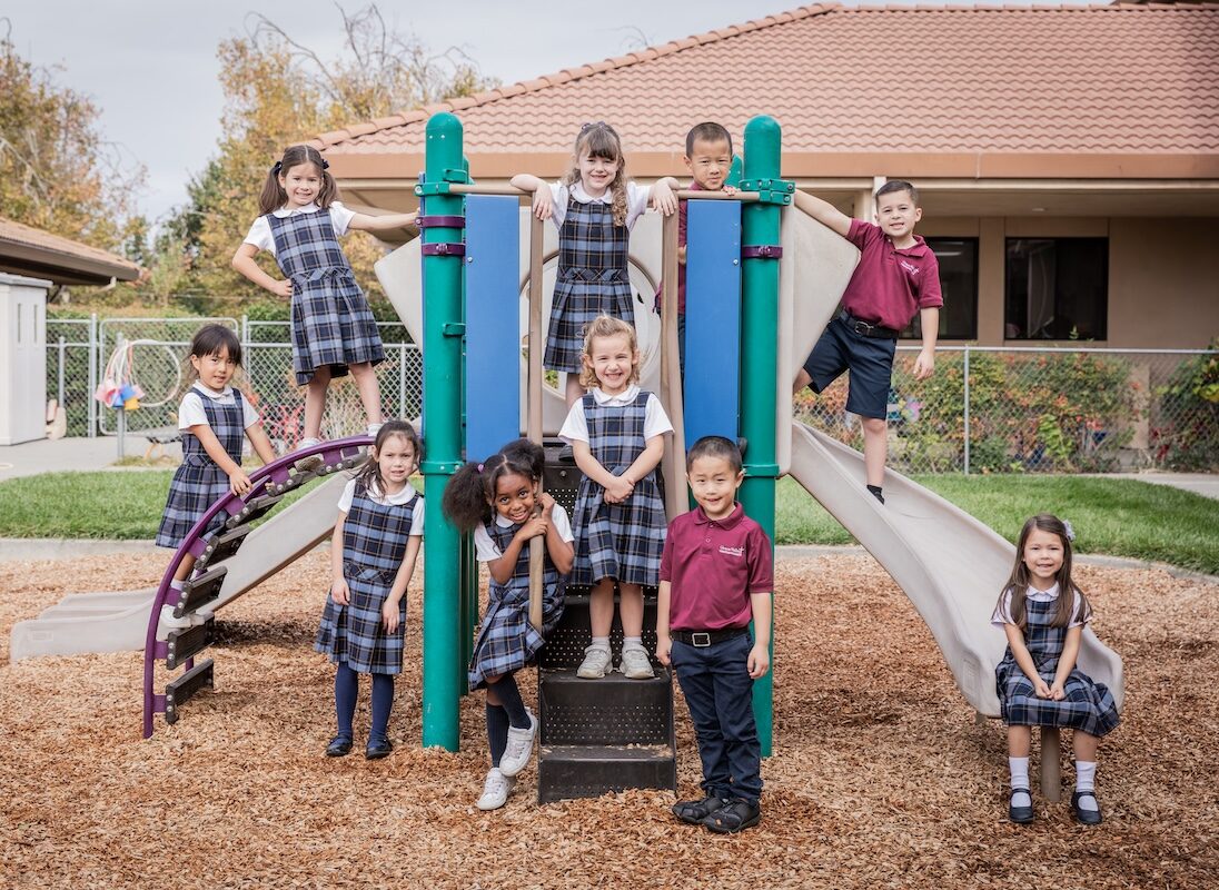 Kingdergarten class poses on the play structure in the Kinder recess yard.