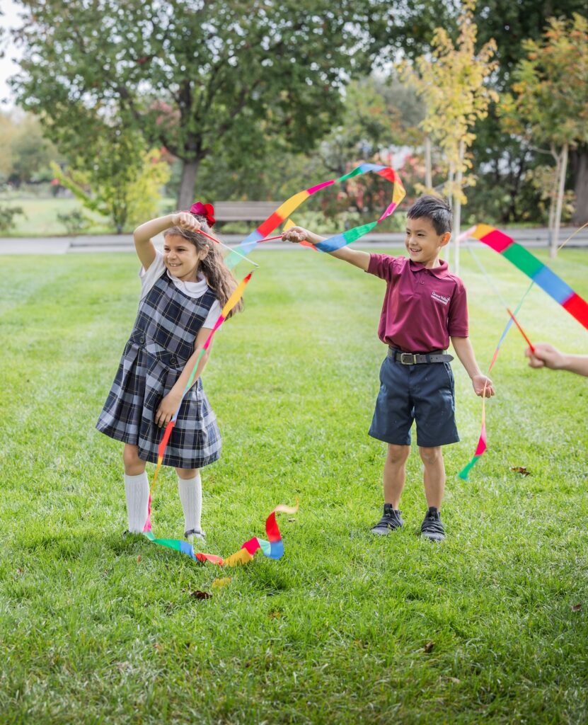 Two elementary students play with colorful ribbons on the school quad.
