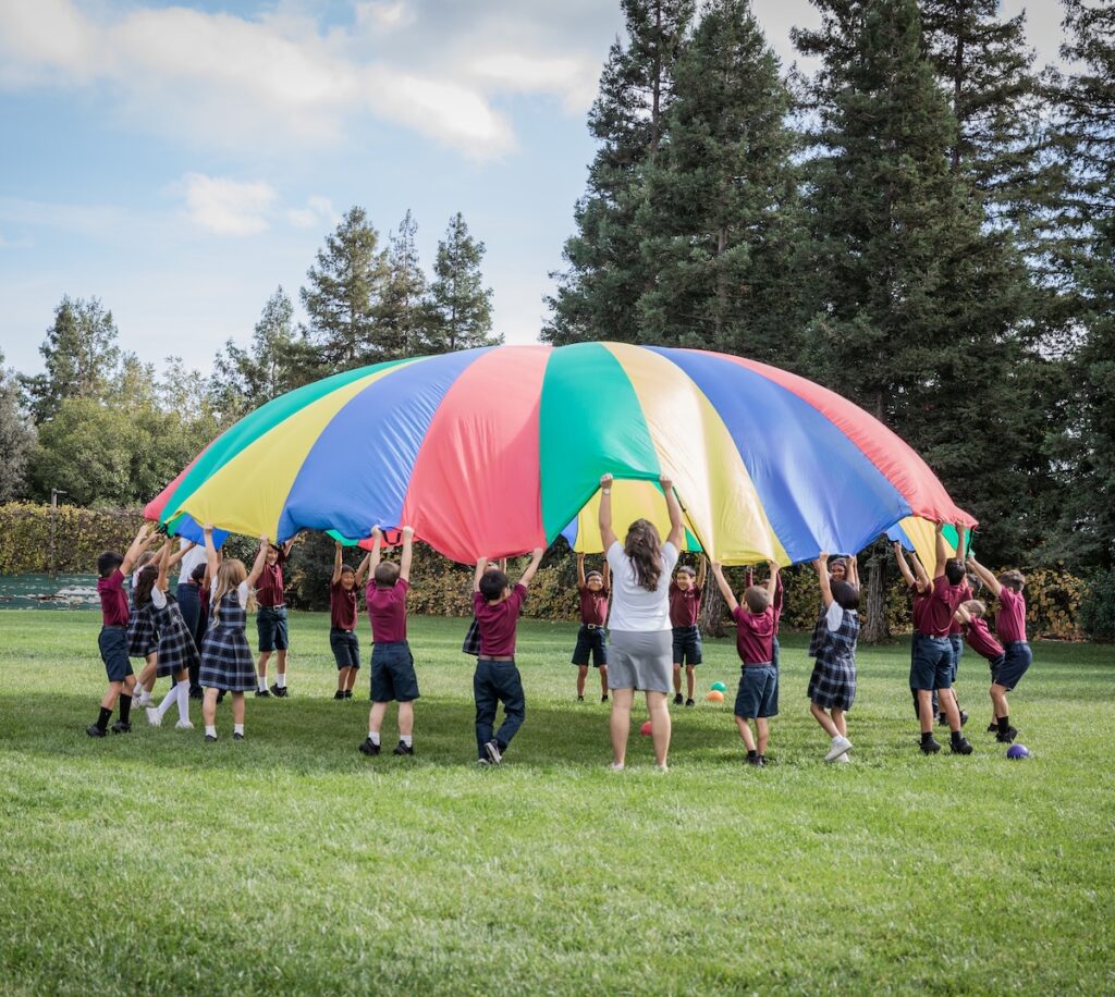 GVCA 2nd and 3rd graders play with balls on a colorful parachute on the backfield of the campus.