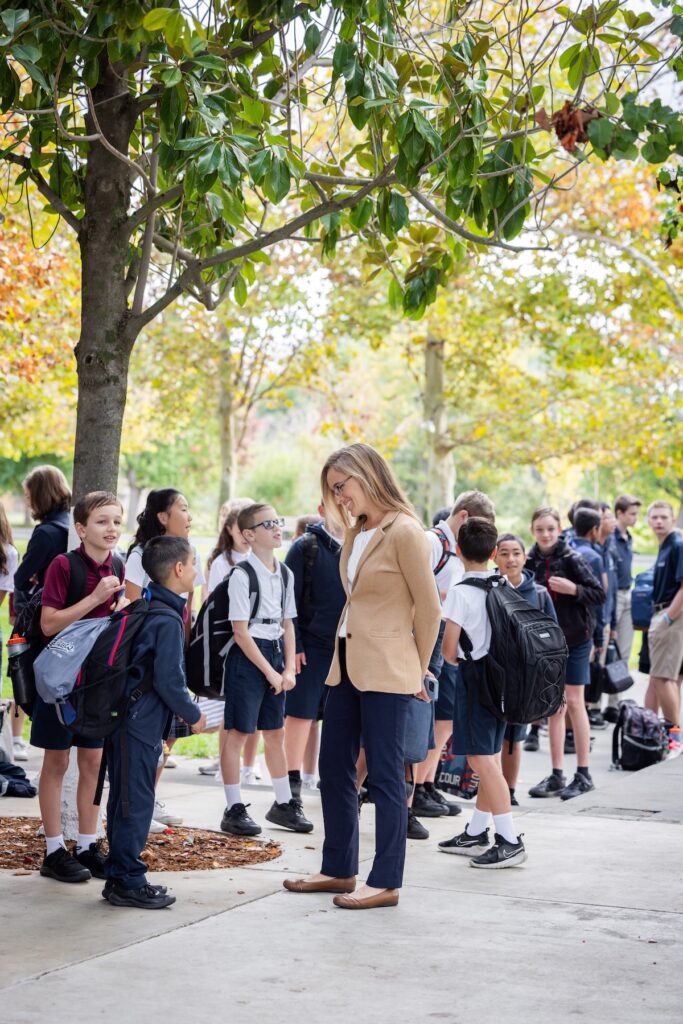 Teacher greets students lined up with their backpacks, eager to start the school day.