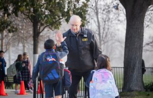 Security guard high fives an excited elementary student during school arrival.